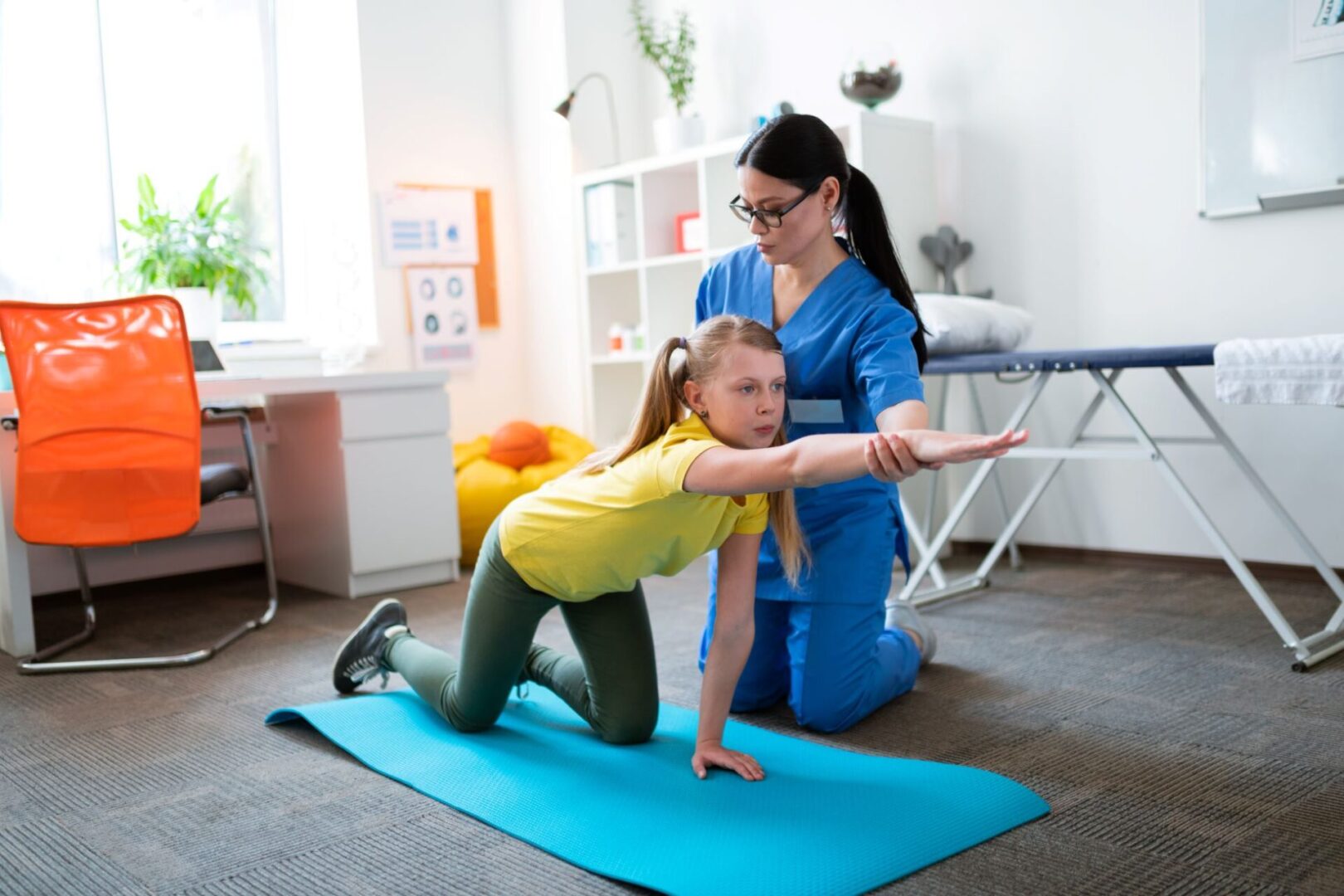 A woman helping a girl do yoga on a mat.